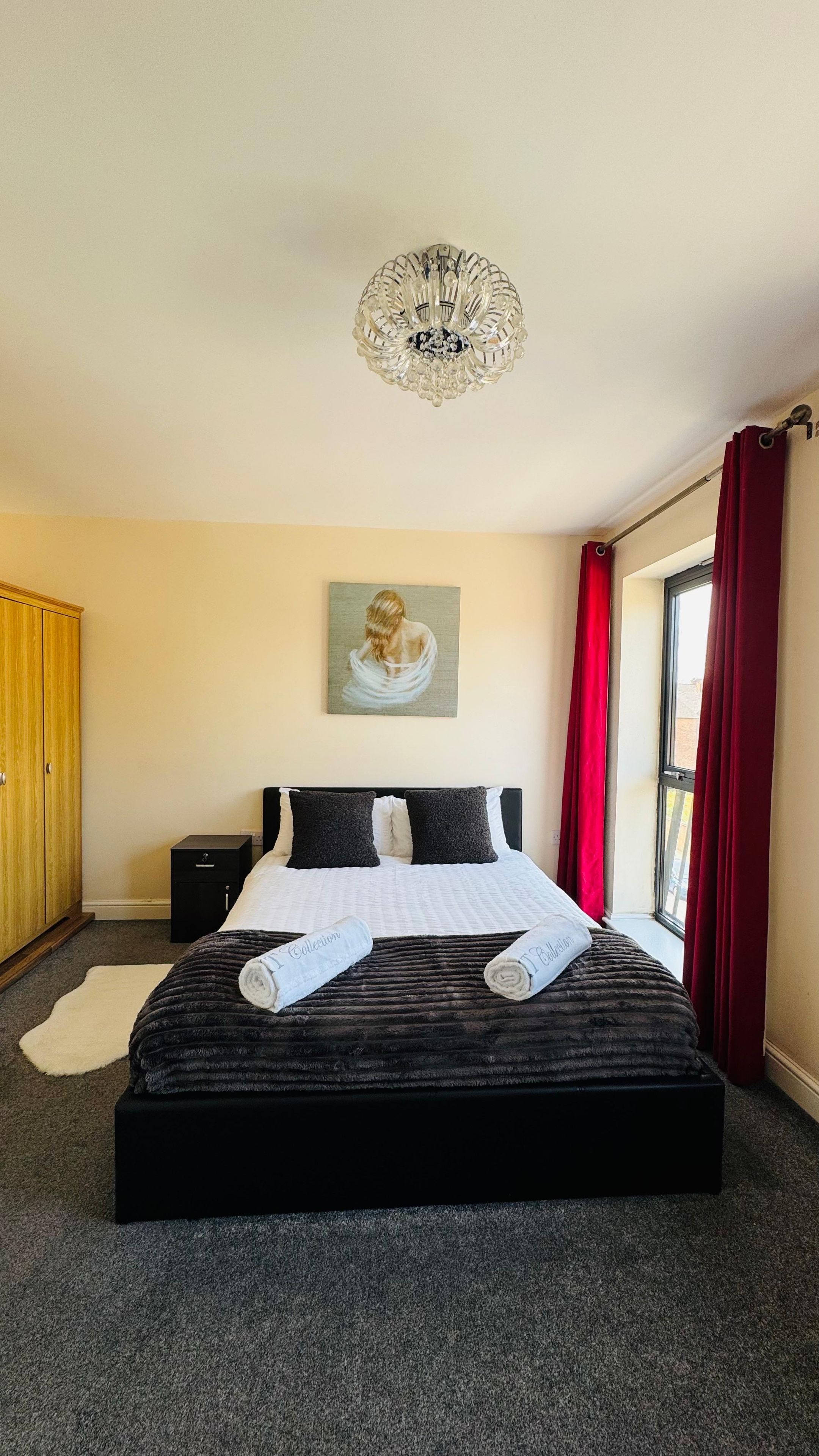 Een hotelkamer met een groot bed, een schilderij aan de muur en een raam met rode gordijnen.