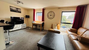 A living room with a sofa, a coffee table, a TV, a dining area with a table and chairs, and a large window with curtains. - Ideal stay for contractors in Wolverhampton. Free parking! Close to city centre! (Wolverhampton)