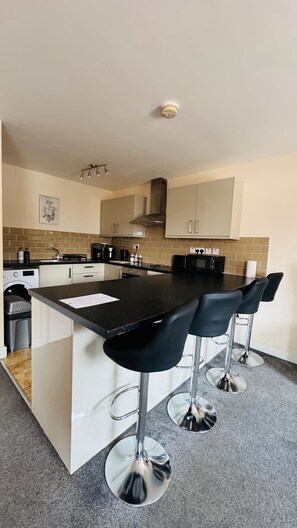 A modern kitchen with a central island, bar stools, and a microwave. - Ideal stay for contractors in Wolverhampton. Free parking! Close to city centre! (Wolverhampton)