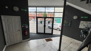 L’entrée d’un hôtel, avec une porte, des panneaux indiquant les issues de secours, un extincteur et une vue sur la rue.