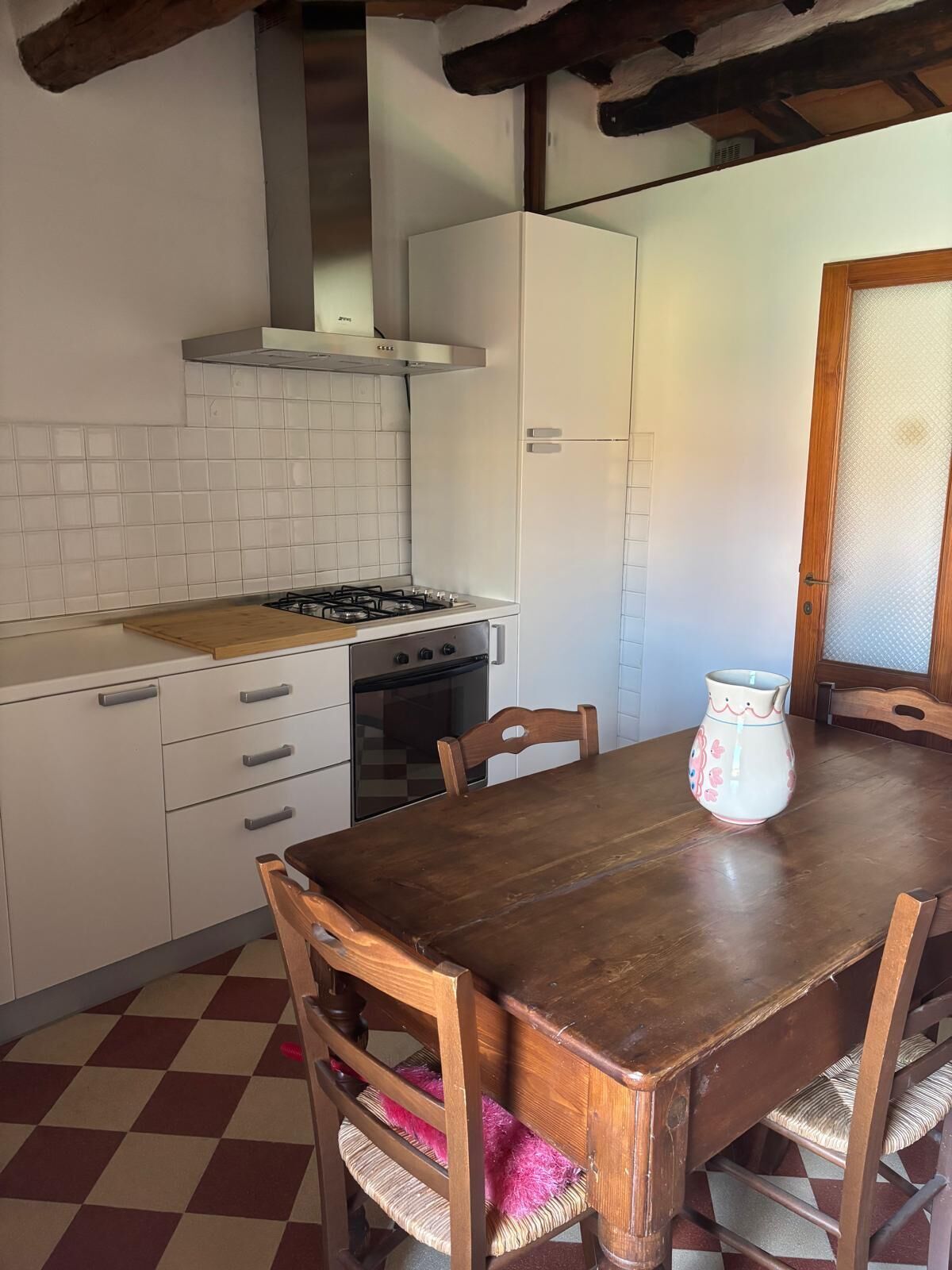 Una cocina con estufa a gas, armarios blancos, una mesa de comedor de madera y una silla con cojín rosa.