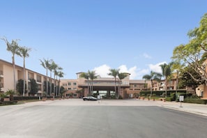 A hotel entrance with a paved driveway, palm trees, and a building with multiple floors and balconies.