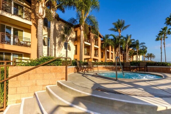 Un hotel con zona de piscina, palmeras y un cielo azul despejado.