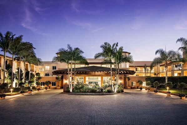 A hotel with a central courtyard, palm trees, and a well-lit entrance.
