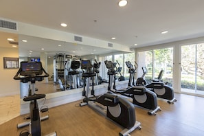 Un gimnasio con máquinas de cardio, un espejo grande y amplias ventanas.