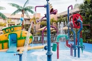 Un área de juegos acuáticos con tobogán, chorros de agua y piscina.