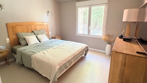 A bedroom with a bed, bedside tables, a desk with a lamp, and a window.