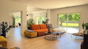 A spacious living room with a sofa, ottoman, coffee table, and a chair. There is a staircase leading to another level, and a large sliding glass door to the outdoors.