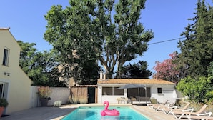 A swimming pool with a pink flamingo float, surrounded by lounge chairs and a pergola.