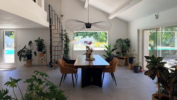 A spacious dining area with a high ceiling, a central table, and chairs. A spiral staircase is visible to the left.