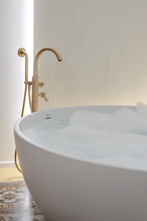 Eine weiße Badewanne mit gebogenem Wasserhahn und Duschkopf, vor einer Wand mit Struktur.