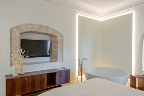Ein modernes Badezimmer mit freistehender Badewanne, einem integrierten Fernseher und einem Steinbogen über dem Waschtisch.
