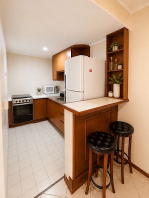 A compact kitchen with a built-in refrigerator, a microwave, a stove, and a small bar area with stools. - Fully equipped apartment in Campinas with pool, gym, and garage. (Campinas)