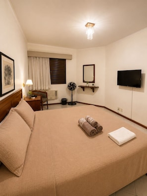 A hotel room with a large bed, a desk, a chair, a fan, a TV, and a ceiling light. - Fully equipped apartment in Campinas with pool, gym, and garage. (Campinas)