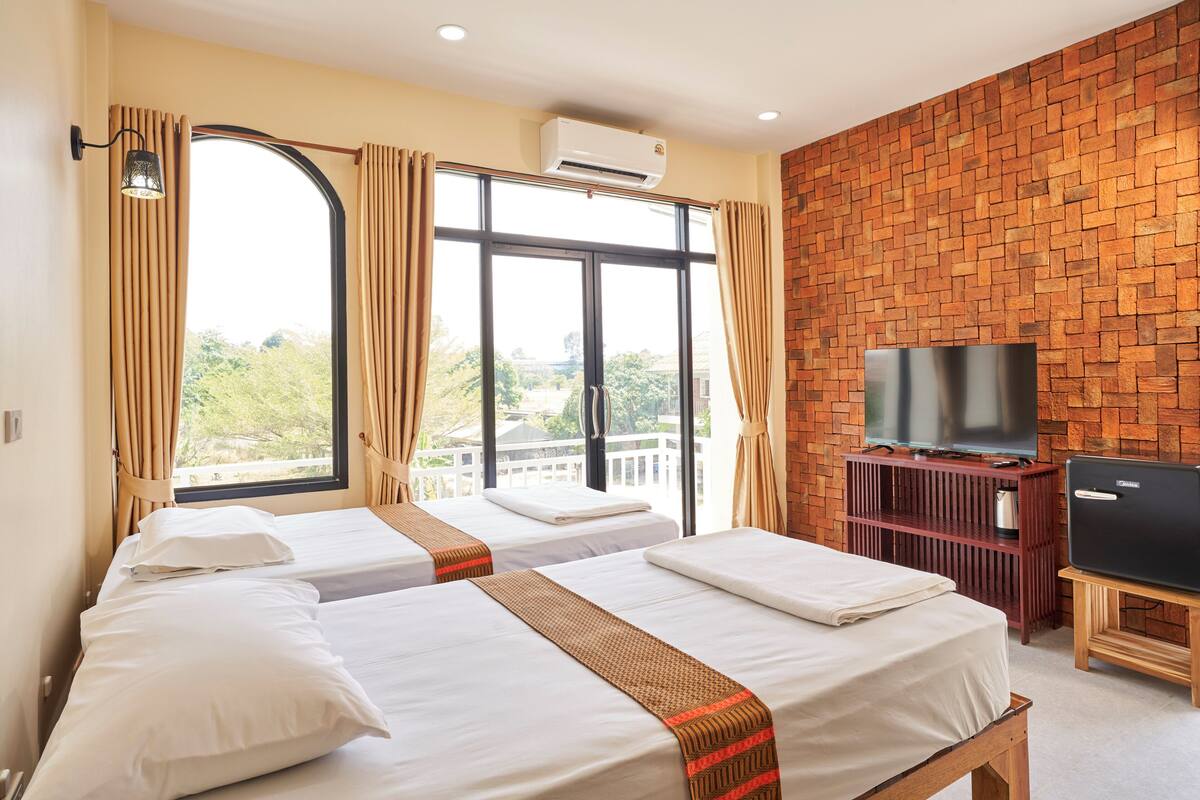 A hotel room with two beds, a TV, an air conditioner, and a brick wall.