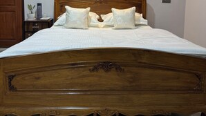 A wooden bed with a headboard, a bedside table with a lamp, and a wall socket.