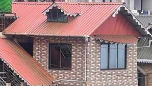 A two-story building with a red roof, a balcony with metal railings, and a window with a curtain.
