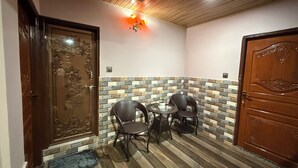 A room with a wooden door, a small round table with two chairs, a potted plant, and a decorative wall with a mix of stone and wood panels.