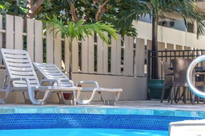 A pool area with white lounge chairs, a dining table, and chairs. - 9th Floor Studio in the Middle of Waikiki (Honolulu)