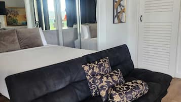 A bedroom with a bed, a black sofa with patterned cushions, a large mirror, and a sliding door.