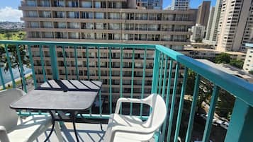 A balcony with a table and chairs, overlooking a cityscape with high-rise buildings.