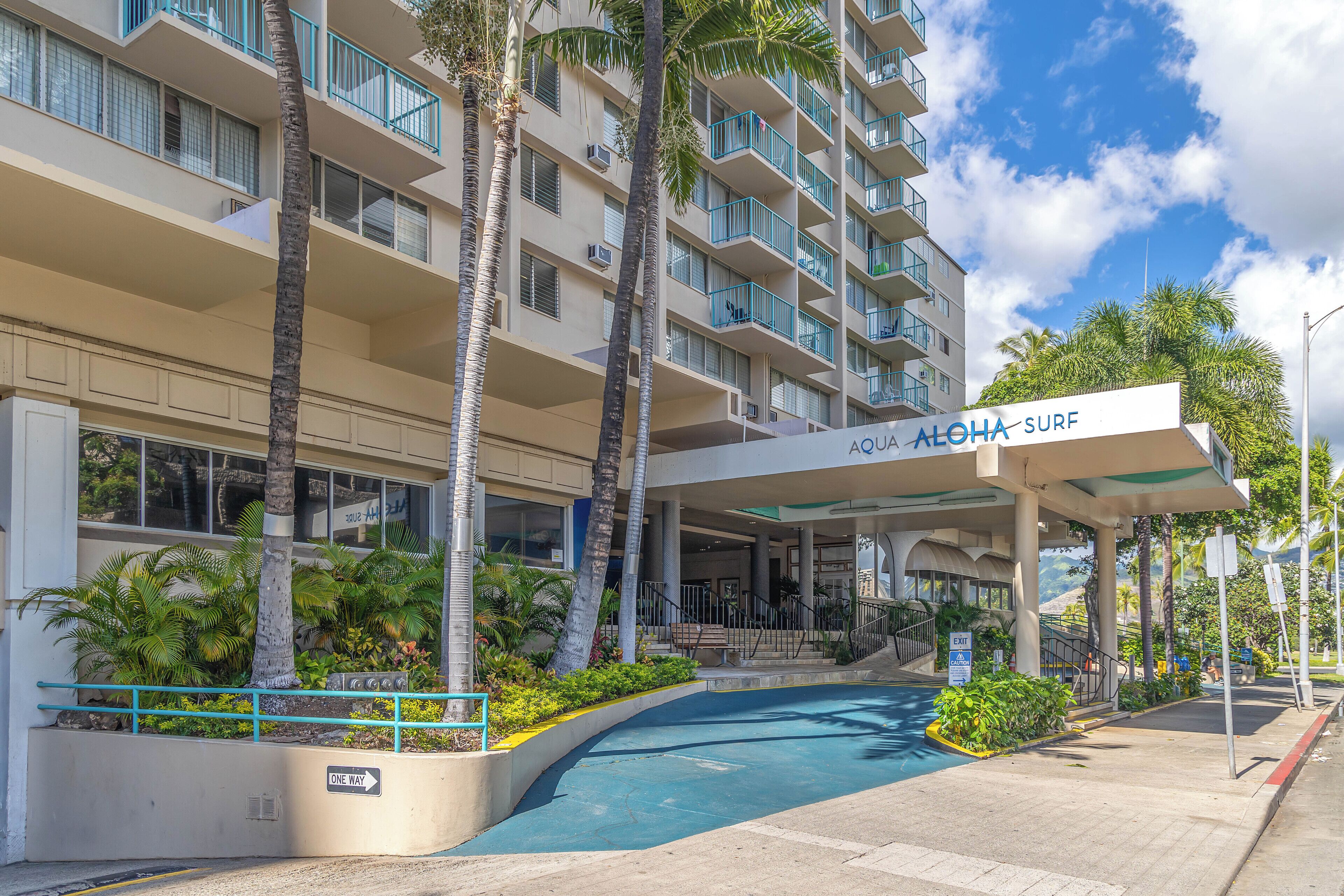 A hotel with a pool area, palm trees, and a sign reading "Aloha Surf".
