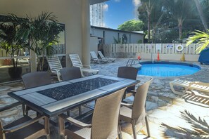 An outdoor pool area with lounge chairs, a table, and potted plants. - 9th Floor Studio in the Middle of Waikiki (Honolulu)