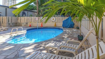 A swimming pool with lounge chairs, a covered area, and a fence with a mural.