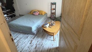 Une chambre à coucher comprenant un lit, une petite table en bois, une étagère avec quelques objets et une armoire.