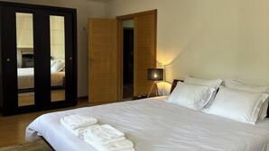 Een slaapkamer met een groot bed, een houten garderobe, een spiegel en een nachtkastje met een lamp.