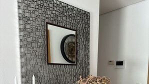 Een modern interieur met een geometrisch wandontwerp, een lijstkastanje klok, een glazen consolese tafel met kaarsen, en een vaas met bloemen.