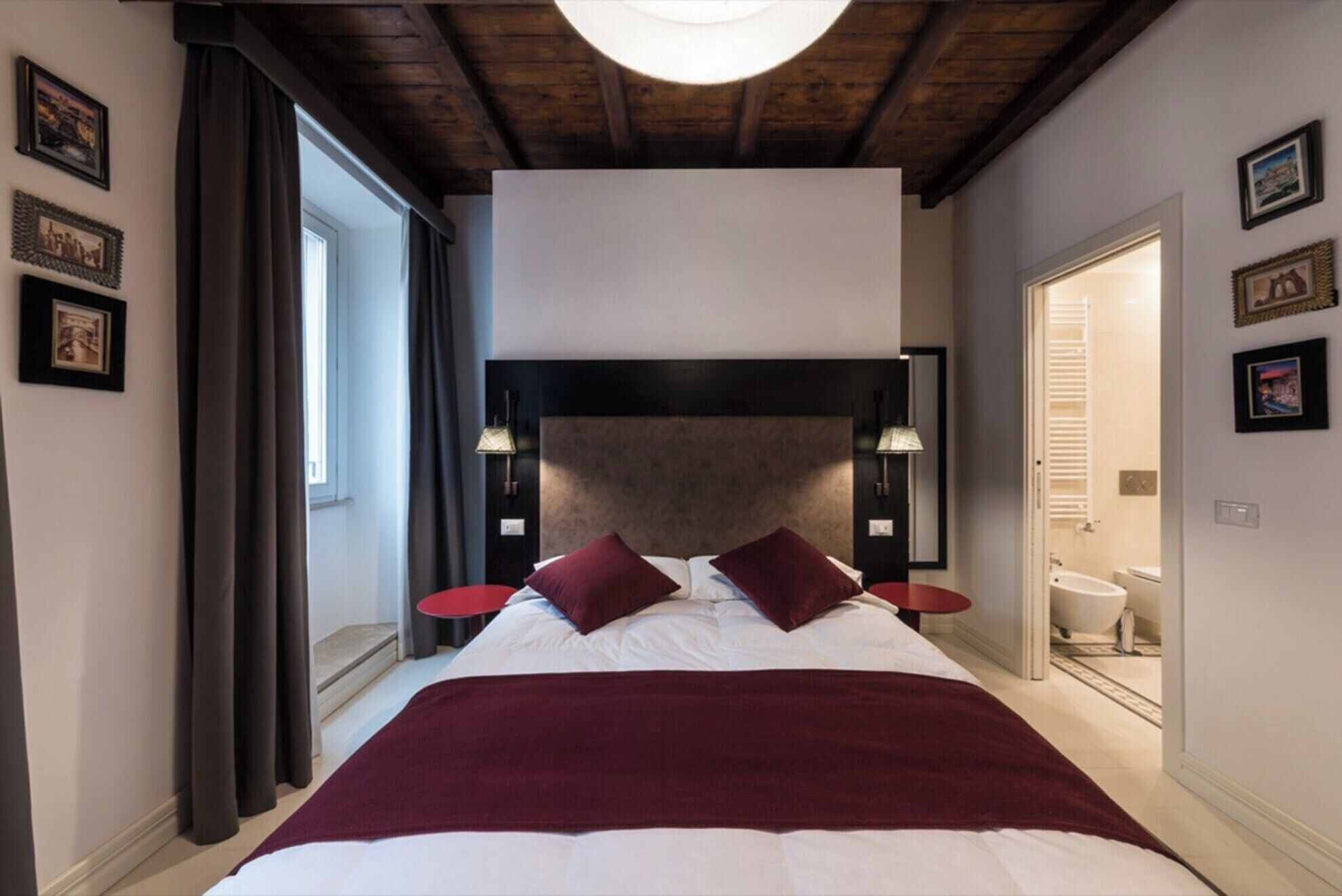 A bedroom with a large bed, two bedside lamps, a headboard, and a view of the bathroom.