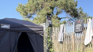A tent with a metal container, a wooden fence, and a tree in the background. - Naéco's Tiny Room (Plouharnel)