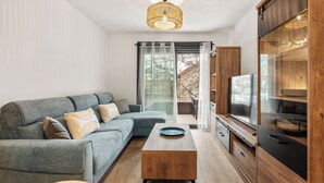Uma sala de estar moderna com um sofá seccional, uma mesa de centro de madeira, uma TV e uma porta de vidro deslizante que dá para uma área externa.