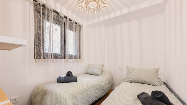 Quarto com duas camas, uma janela com cortinas estampadas e um lustre no teto.