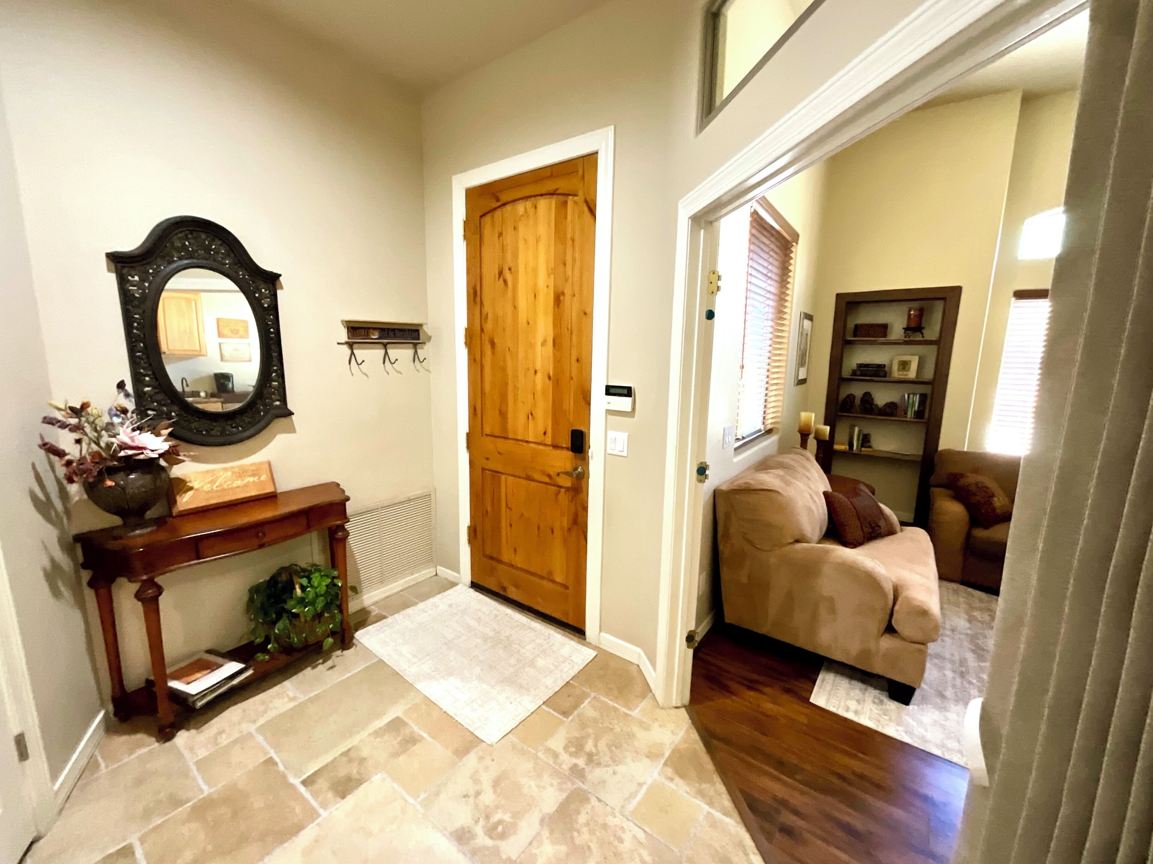 A hallway with a wooden door, a console table with a vase, a mirror, and a rug.