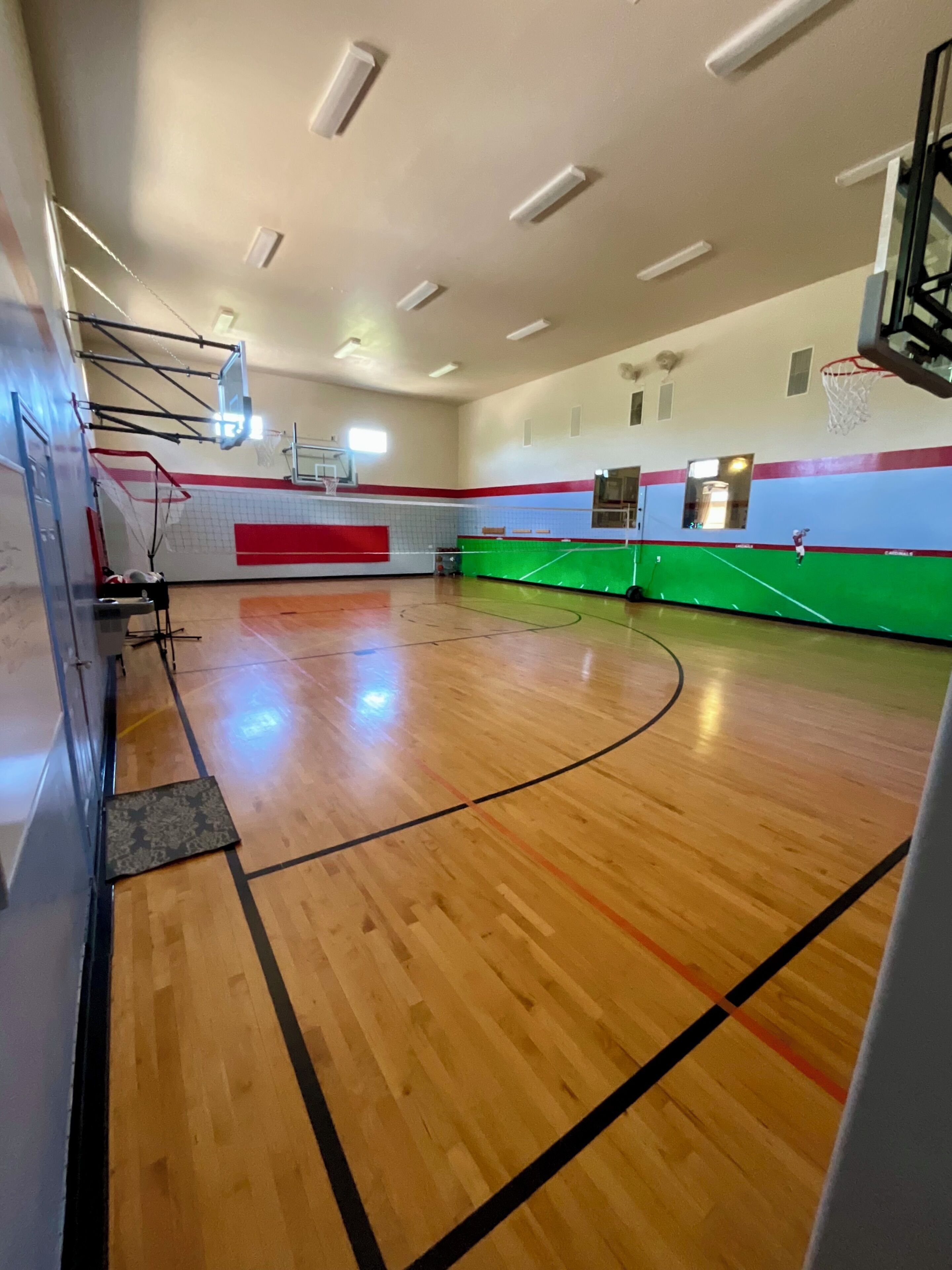 Een basketbalveld met een houten vloer, een basketbalring en een volleybalnet.