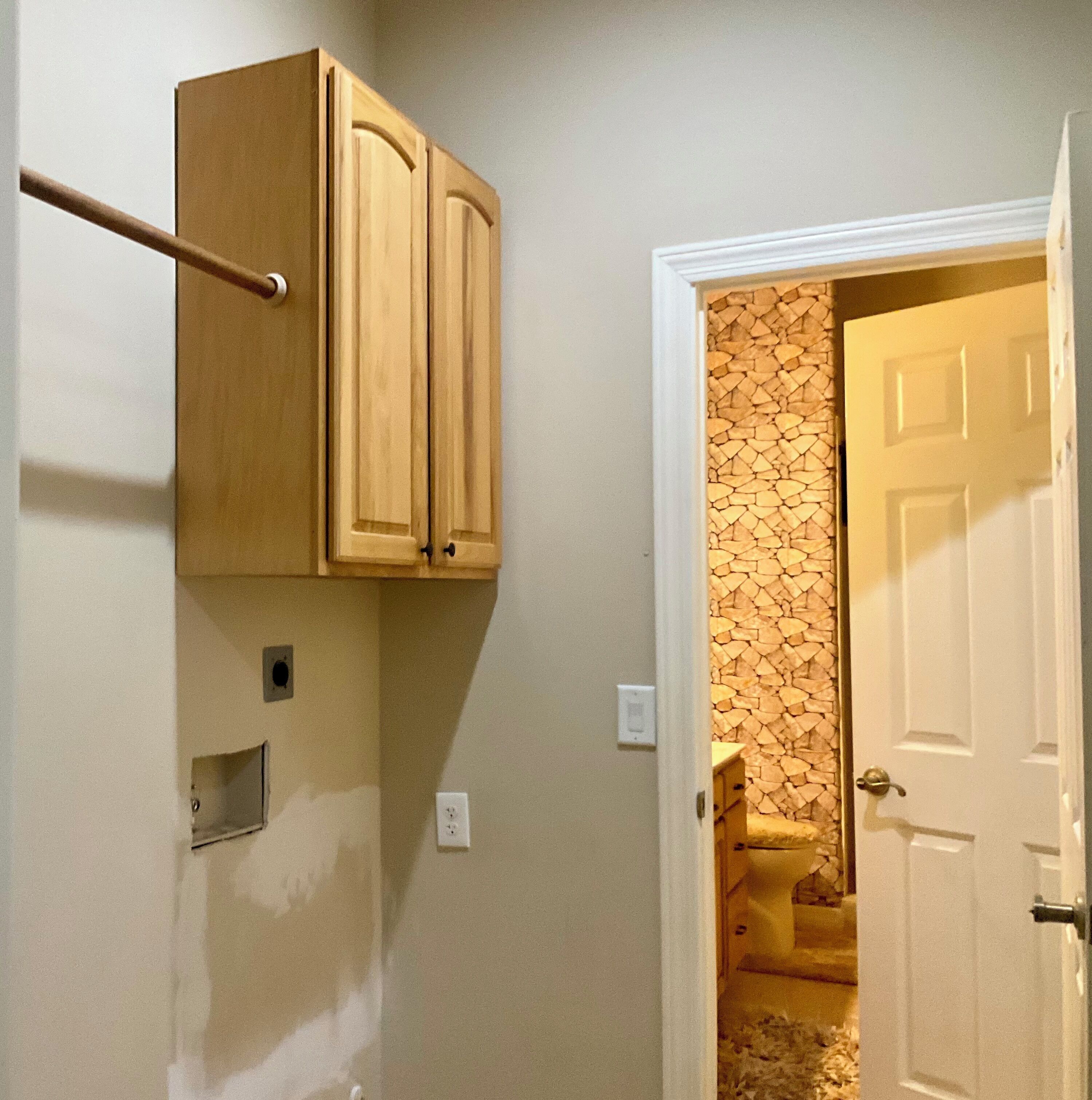 A room with a wooden cabinet, a white door, and a wall with a stone-like pattern.