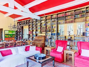 A library with bookshelves, a red armchair, a white sofa, and a chandelier. - Grenouille by Interhome (Vence)