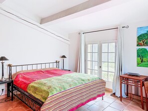 A bedroom with a bed, a nightstand, a lamp, a window with curtains, and a painting on the wall. - Grenouille by Interhome (Vence)