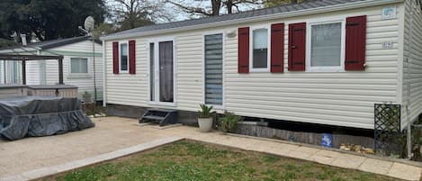 Une maison mobile dotée d’un patio couvert, d’un petit porche à l’avant et d’une antenne parabolique.