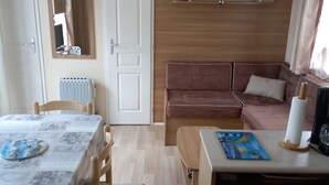 Ett kompakt bostadsutrymme med ett matbord, en soffa, ett litet köksområde och en spegel.