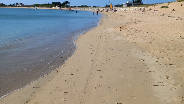 En strand med klart, blått vatten, en sandstrand och några få personer i fjärran.