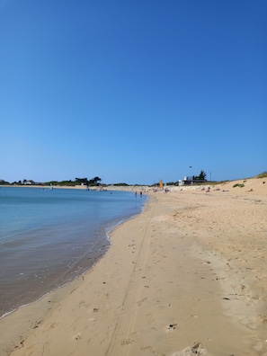 Ein Strand mit klarem, blauem Wasser, sandigem Ufer und ein paar Personen in der Ferne.