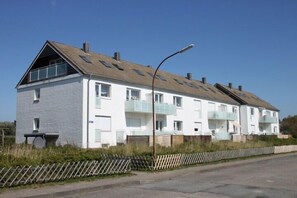 Ein zweistöckiges Wohngebäude mit Satteldach, mehreren Balkonen und einem Eingang zur Straße.