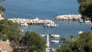 Uma marina costeira com barcos atracados, molhes rochosos e o horizonte de uma cidade ao longe.