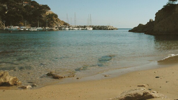 Uma praia com águas claras, barcos e falésias rochosas.