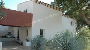 Uma casa moderna de dois andares com telhado plano, paredes externas brancas e um deck de madeira.