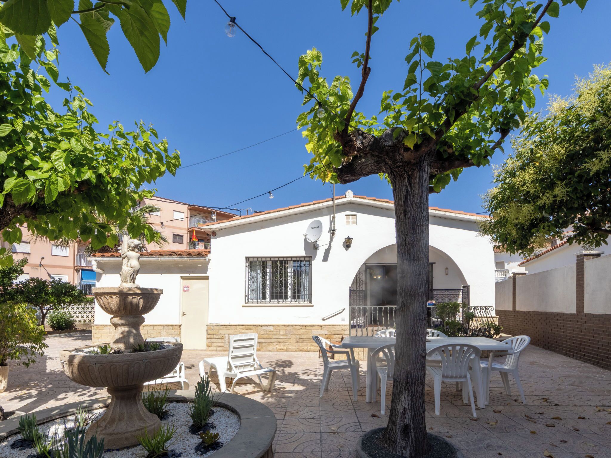 A courtyard with a white building, outdoor seating, and a fountain.