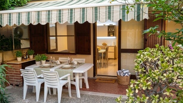 A patio with a table set for four, surrounded by white chairs, and a striped awning above. - Apartment by the Sea (Marina di Davoli)